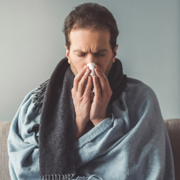 man wrapped in blanket blowing his nose