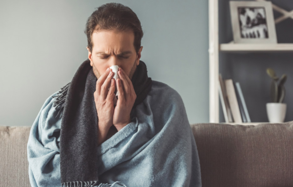 man wrapped in blanket blowing his nose